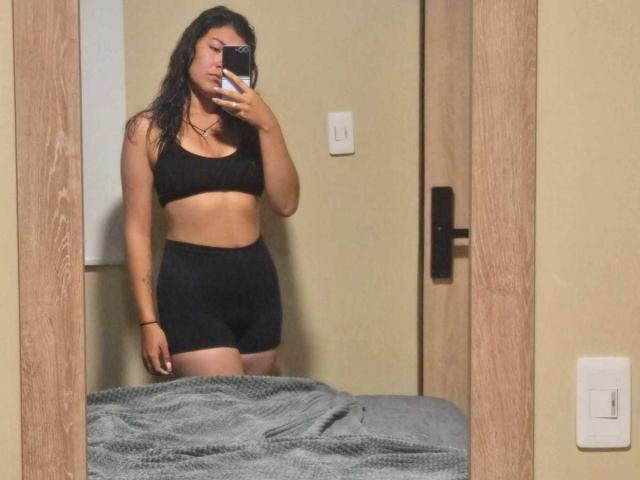 ValeryMartinez with wet black hair, wearing a black sports bra and black shorts, taking a mirror selfie, showing her toned ass and small tits, standing in a bedroom.