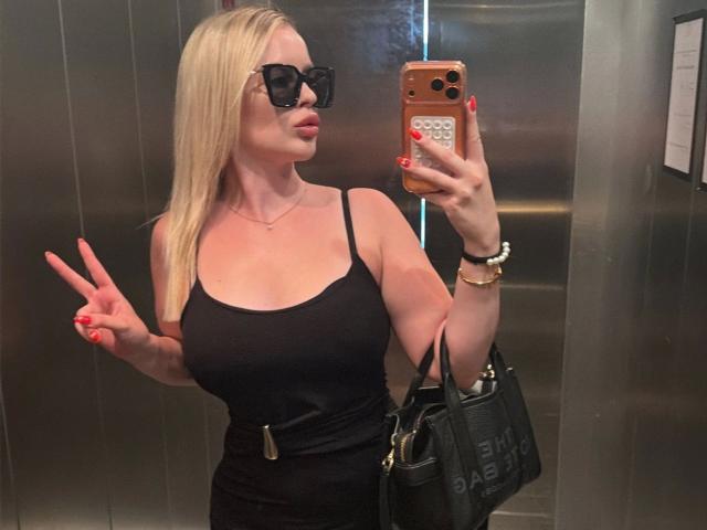 Hellybunny-hot with blonde hair, black tank top, big boobs, black sunglasses, red nails, smartphone, black handbag, and peace sign in elevator mirror selfie.