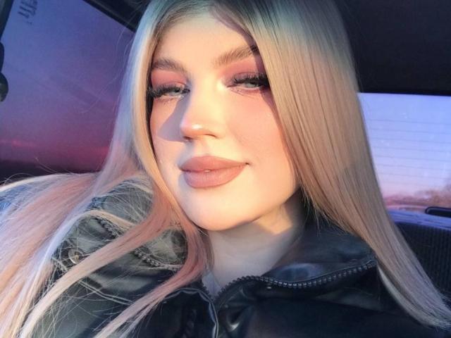 Tawanna Lehrman, met lang blond haar, roze oogschaduw en volle, roze lippen, draagt een zwarte leren jas en glimlacht in een auto..