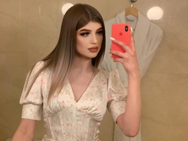 Tawanna Lehrman, met lang bruin haar, gekleed in een bloemenjurk, houdt een rode telefoon vast en maakt een spiegelzelfportret, waarbij ze haar volle lippen en witte nagels laat zien..