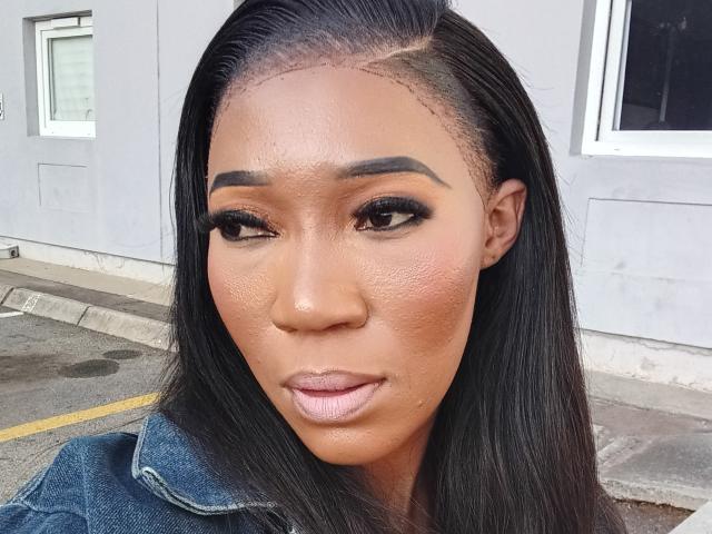 TeeGlam heeft een glanzend bruin gezicht met dikke, zwarte wenkbrauwen, lang zwart haar, en draagt een denimjas. Haar make-up omvat donkere eyeliner en roze lippenstift..