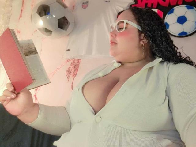 HurrenMatt, fat with large tits, wearing white cardigan, glasses, and pink blush, reading book, black curly hair, soccer ball and soccer shirt in background, lying on bed.