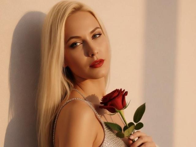 MyaHott with long blonde hair, red lipstick, and a red rose, holding it against her chest, wearing a sparkly dress, looking seductively at the camera.