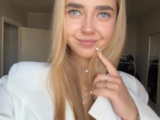 Georgine Branen, avec ses cheveux blonds, ses yeux bleus et son petit sourire, portant une veste blanche, touchant sa joue avec un doigt, montrant une bague, sur une photo de profil..