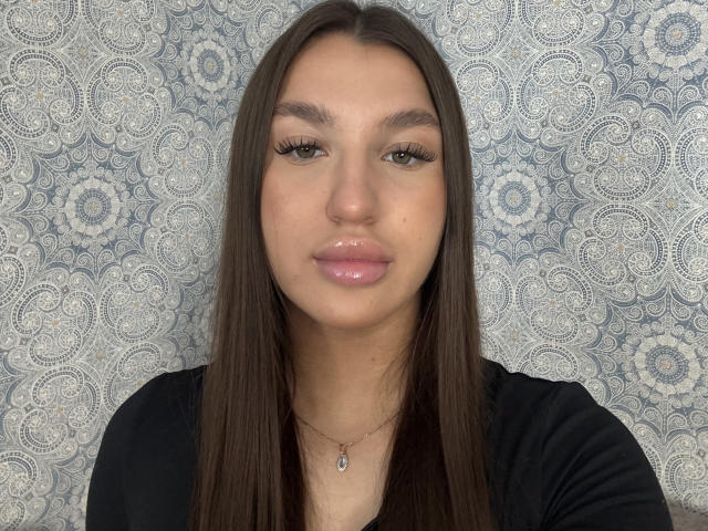 Ingeborg Wheadon tiene labios rosados y brillantes, cabello castaño largo y pestañas gruesas, y lleva una camisa negra con un collar de plata, mirando directamente a la cámara..