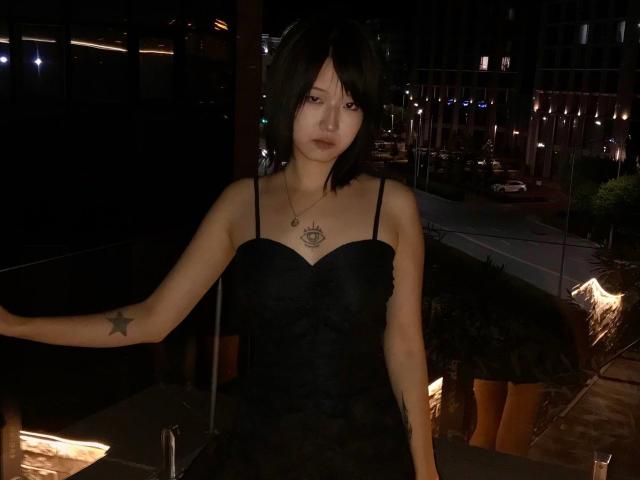 Kayce Molinas, con i capelli neri e corti, indossa un abito nero con lacci e ha un tatuaggio a forma di stella sul braccio destro e una collana con un occhio, ed è in piedi in una scena notturna urbana, scarsamente illuminata..