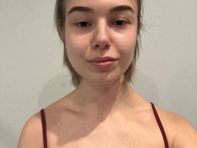 Slyvia Coffen hat ein süßes Gesicht mit kleinen, braunen Augen, heller Haut und braunen Haaren, die zu einem unordentlichen Pferdeschwanz gebunden sind. Sie trägt ein rotes Top mit Spaghetti-Trägern, das ihre Brüste zeigt..