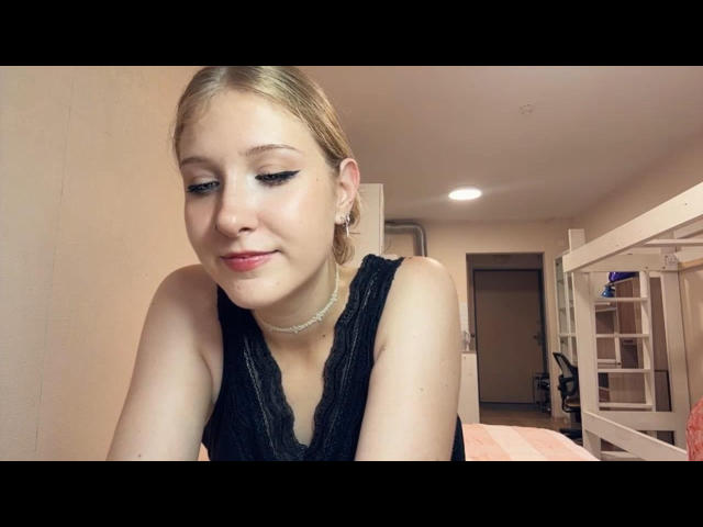 OpalMccullars mit blonden Haaren, schwarzem Eyeliner, kleinen Brüsten und einem süßen Lächeln, trägt ein schwarzes Top ohne Ärmel und eine Halskette, in einem Schlafzimmer mit einem weißen Etagenbett..
