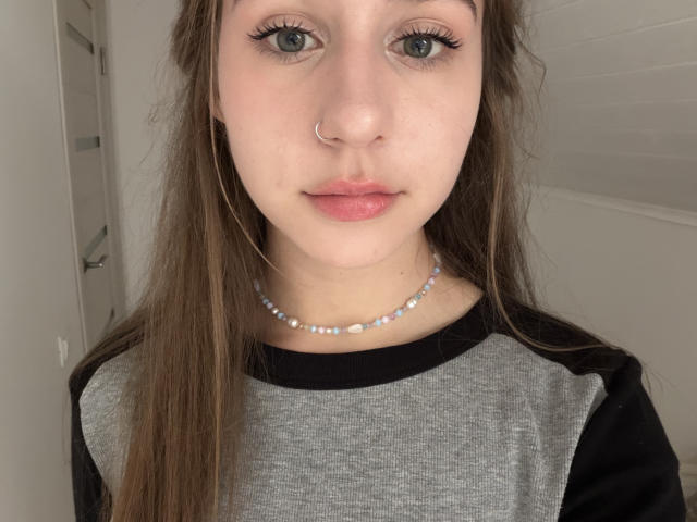 KathrynMasson has gray eyes, long brown hair, a nose ring, and a beaded necklace. She's wearing a gray and black raglan shirt with pinkish lips.