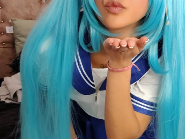 YayaLm, com rabos de cavalo azuis vibrantes, lábios carnudos, vestindo um uniforme de marinheira azul e branco, com a mão levantada, pulseira rosa, fofa, mostrando os seios, unhas rosa claras..