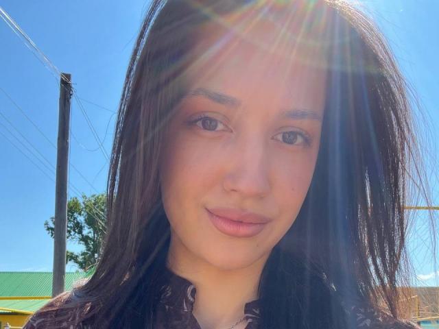 AdrianneRossey's face with sunrays, brown hair, and pink lips, wearing a black top, blue sky background, and a power line on the left. Her ass is not visible.