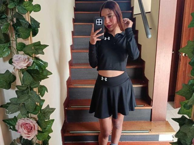 Valerie Woods, met een medium bruine huid, rode lippenstift en recht bruin haar, draagt een zwart Under Armour topje en rok, staat op houten trappen en houdt een smartphone vast..