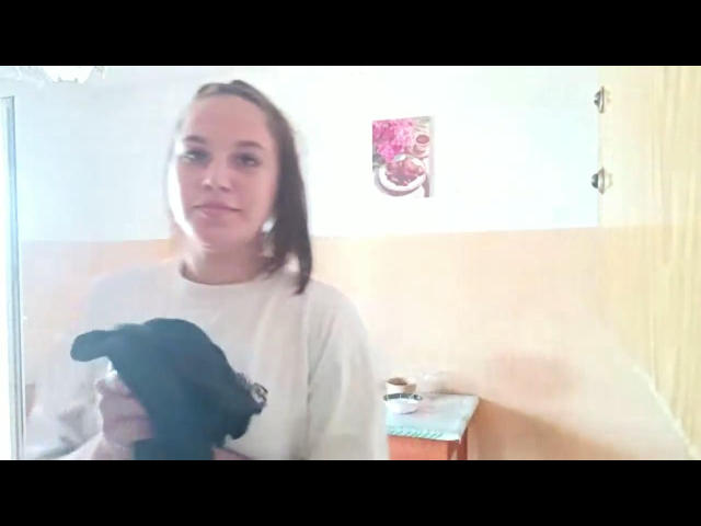 WinnieFalso che tiene tra le braccia un piccolo cucciolo nero, indossa una camicia bianca, ha i capelli castani e un'espressione neutra, in una stanza molto luminosa..
