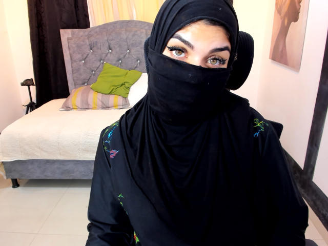 Aniisa Ali, met donkere ogen, draagt een zwarte hoofddoek en boerka, waarbij haar ogen en bovenste borst zichtbaar zijn. Haar kleding is versierd met kleurrijke borduursels. Ze zit in een slaapkamer..