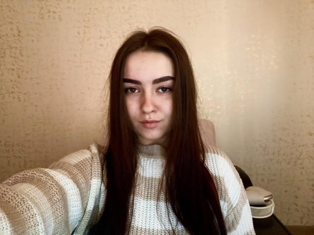 Onita Waltemath hat langes, braunes Haar, dicke Augenbrauen und trägt einen gestreiften, weißen und grauen Pullover. Sie schaut mit einem leichten Lächeln in die Kamera. Ihre Nase ist durchstochen..