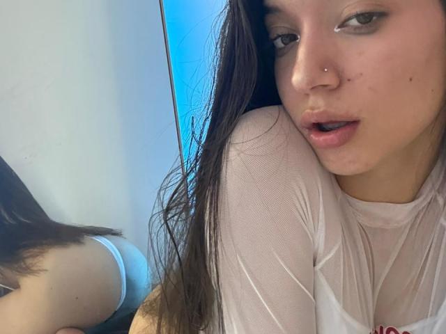 MichellFord has long brown hair, a nose piercing, and a slightly open mouth. She's wearing a wet white shirt, showing her butt in white underwear in a mirror reflection.