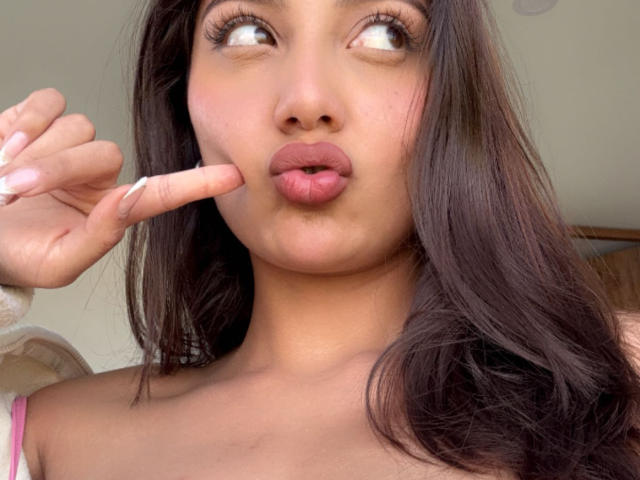 DianaFernandezz, con le labbra tumefatte, occhi marroni che guardano verso l'alto e un dito vicino alla bocca. Ha lunghi capelli castani, pelle color nocciola e rossetto rosa. Il suo seno è parzialmente visibile..