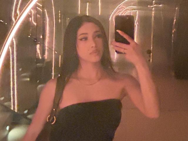 NashiroSakuraii with long dark hair, wearing a black strapless top, holding a phone, taking a mirror selfie, showing a subtle pout, and a small necklace.