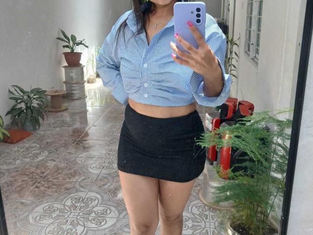 SolaraDubois in a blue striped shirt, black skirt, and no pants showing her bare ass, holding a phone in a mirror selfie, standing on a tiled floor.