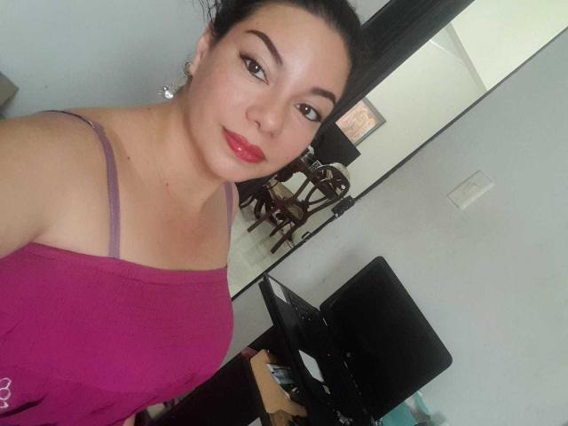 HypnoticBella has large tits, wearing a pink spaghetti-strap top, red lipstick, dark hair in a bun, and is looking at the camera with a slight smile.