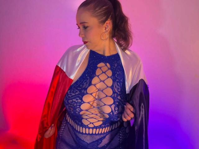 MirandaDelacroix with brown ponytail, wearing blue lace-up dress, exposing large boobs, red and white satin robe, purple and pink lighting, looking to the side, holding robe.