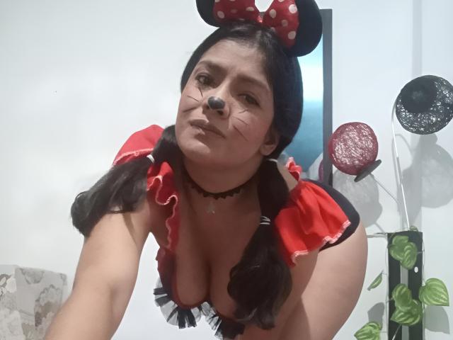 ArianithaXox with black nose makeup, red puffed sleeves, and black Minnie Mouse ears, bent forward, showing her tits, black choker, and pigtails, in a playful, sexy costume.