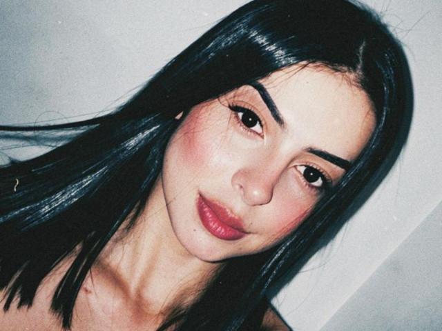 IsabellaJames has dark, straight hair, full pink lips, and arched eyebrows. Her brown eyes are slightly downcast, with a soft, confident smile on her face.