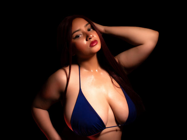 GraceBlue69 com pele brilhante e úmida, vestindo um top de biquíni azul, seios grandes, mão no cabelo castanho comprido, fundo escuro, lábios vermelhos, confiante, sexy, brilhante, atraente..