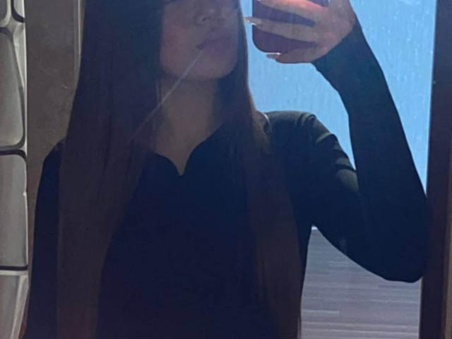 LangGalicia ha lunghi capelli castani, indossa una camicia nera a maniche lunghe e sta scattando un selfie allo specchio con il telefono, mostrando solo il suo viso e la parte superiore del corpo..
