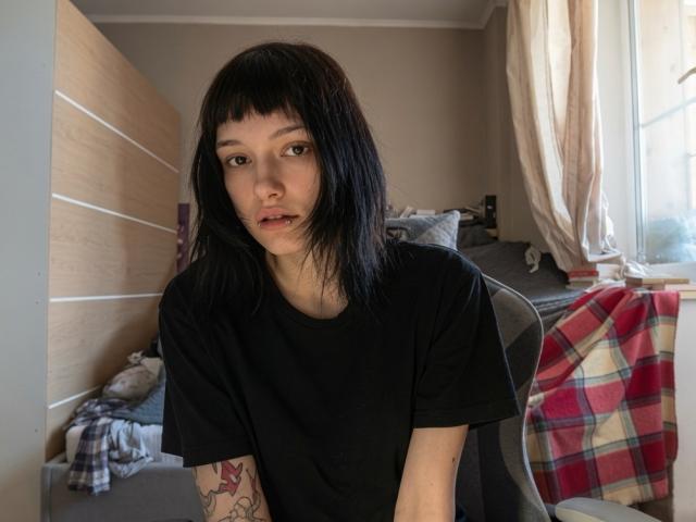 Valery Bazzle, mit schwarzen, schulterlangen Haaren, trägt ein schwarzes T-Shirt und hat ein Tattoo auf ihrem linken Arm. Sie sitzt auf einem Stuhl, blickt in die Kamera und hat einen kleinen Schnitt auf ihrer Lippe..