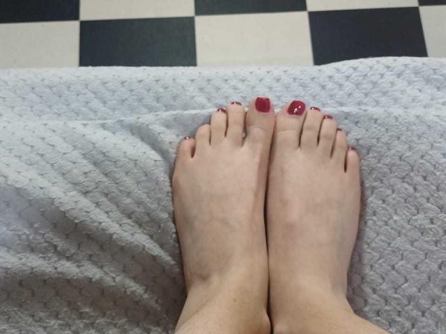 Los pies de KatalinaLaurent, con las uñas de los dedos de los pies pintadas de rojo, descansando sobre una toalla blanca texturizada, con los dedos ligeramente separados, sobre un suelo a cuadros blancos y negros..