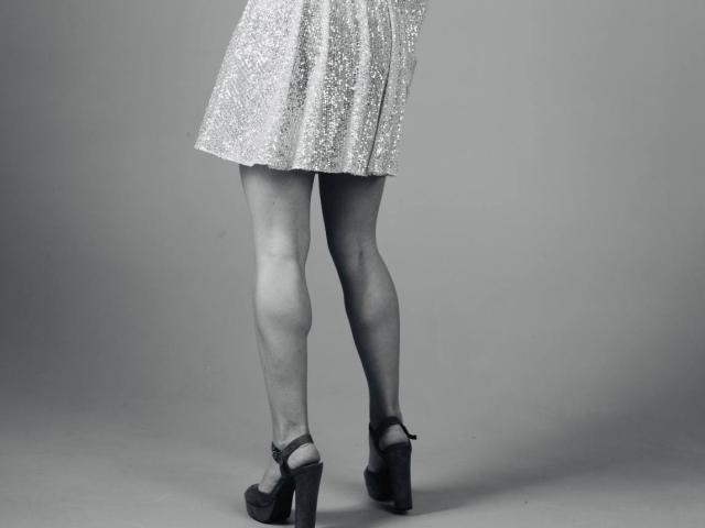 Le gambe di BalletSwan, che indossa una gonna scintillante e scarpe con plateau nere e tacchi alti, sono leggermente divaricate, mostrando una leggera flessione nel ginocchio destro..