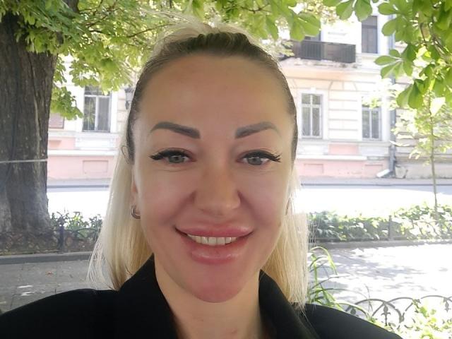 MysteryLaddy a les cheveux blonds, des sourcils foncés, de longues cils noirs et un joli sourire. Elle porte un haut noir avec des lèvres roses et de petites boucles d'oreilles..