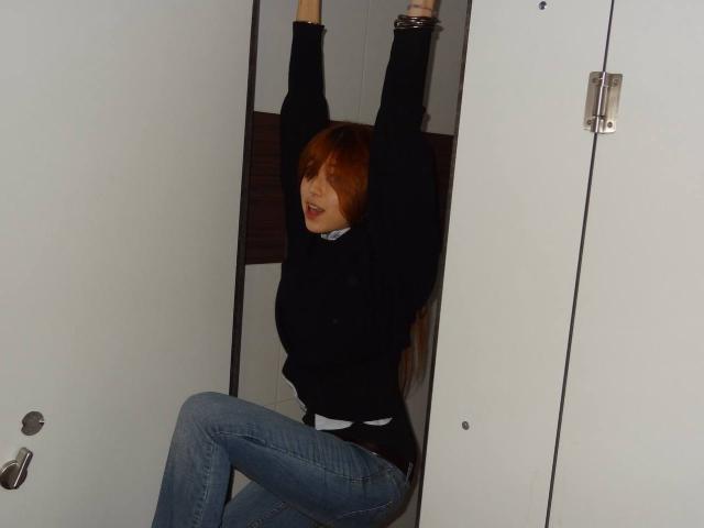 Arlena Stinnett, avec ses cheveux roux, son pull noir et son jean bleu, est menottée, les bras au-dessus de la tête, assise par terre, et a l'air bouleversée. Ses fesses sont visibles..