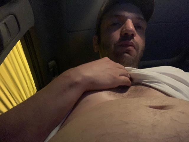 El pecho de Meshuuggeettaa, con una mano levantando una camisa, mostrando un abdomen peludo y ligeramente abultado, con un ombligo visible. Lleva un gorro y está mirando a la cámara..