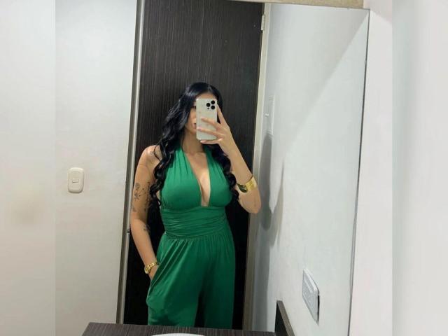 IsabellaJames with large tits, wearing a green halter romper, long black hair, gold bracelet, and phone covering her face, standing in a bathroom, looking in a mirror.