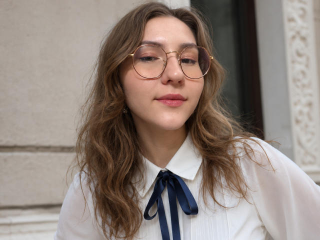 LenoreSchontz heeft golvend bruin haar, draagt een bril met gouden rand en een witte blouse met een marineblauwe strik. Ze heeft roze lippen en een subtiele glimlach. Haar borsten zijn klein..