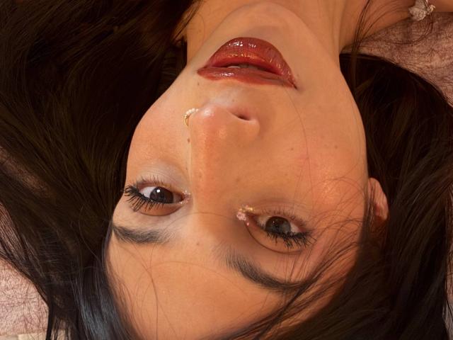 SophieBeaumont's face, upside down, with shiny red lips, black eyelashes, and a tiny boogers on her nose. She has brown eyes and dark, wavy hair.
