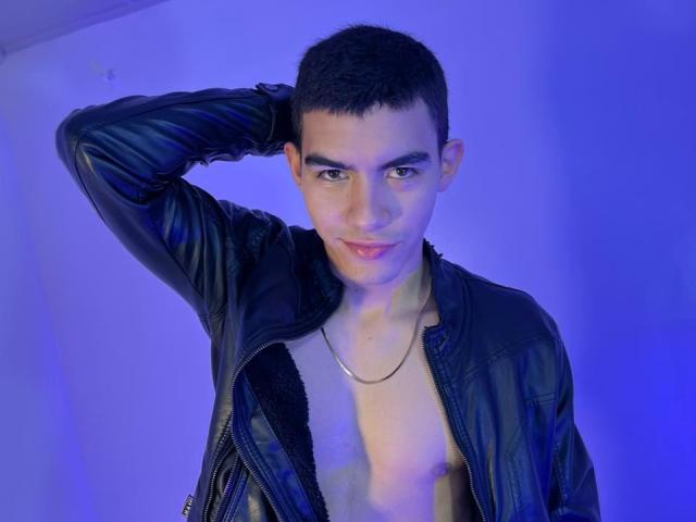 SebastiianVega, short dark hair, black leather jacket, no shirt, showing chest, hand behind head, blue lighting, silver necklace, slight smile, confident, cute, looking at camera.