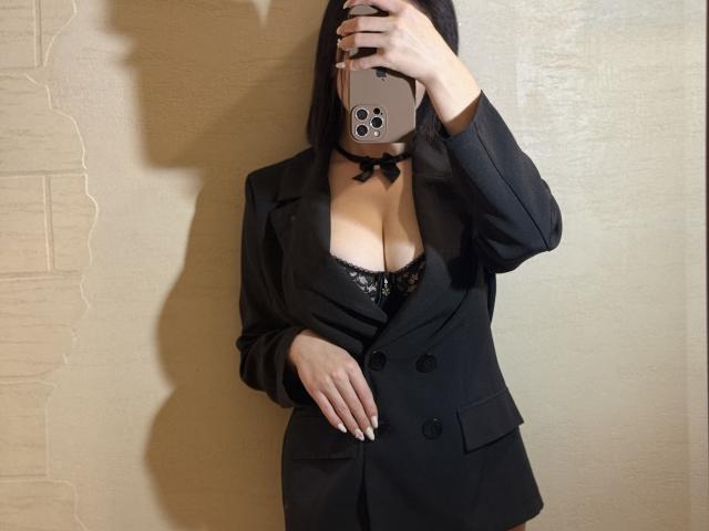 EmmaNoa taking a mirror selfie, wearing a black blazer with her tits showing in a black lace bra, choker, and long nails, holding a gold phone.