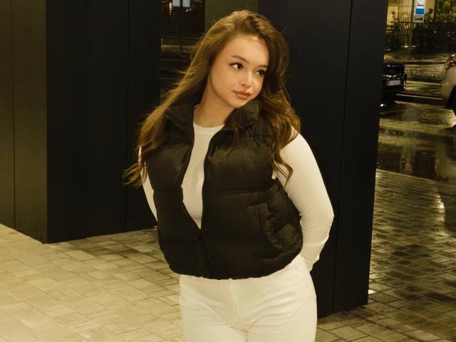 Tawnya Kaczmarski, avec de longs cheveux bruns, un haut blanc, un gilet noir matelassé, les mains dans les poches, debout dans une zone urbaine humide et faiblement éclairée, regardant légèrement sur le côté..