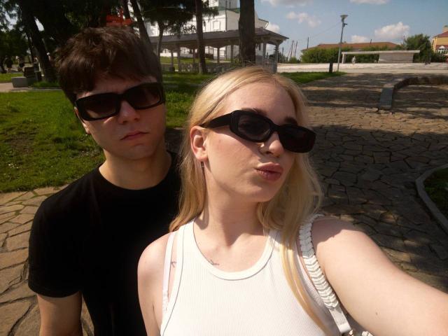 A selfie of LessieKirtner with a dude, both wearing black sunglasses. She's got blonde hair, pouty lips, and a white tank top. He's in a black tee.