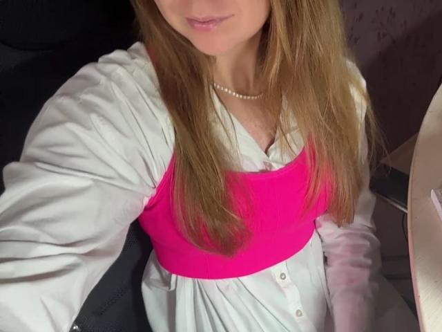 La selfie de Ardelia Amesbury la muestra con cabello largo y castaño, un sostén rosa, una camisa blanca y un collar de perlas. Sus senos son visibles debajo del sostén rosa. Está en un coche..