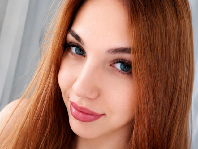 FarahSings tiene el pelo rojo, ojos azules y lápiz labial rosa, y sonríe a la cámara con los senos ligeramente visibles debajo de su camisa. Su maquillaje es impecable, y se ve sexy..
