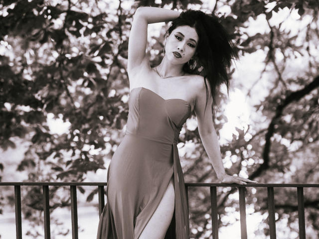 Nashiro Sakurai est debout, vêtue d'une robe fendue sur le côté, son bras levé, exposant ses fesses, sur une photo en noir et blanc où ses cheveux noirs flottent, avec une rambarde en métal..