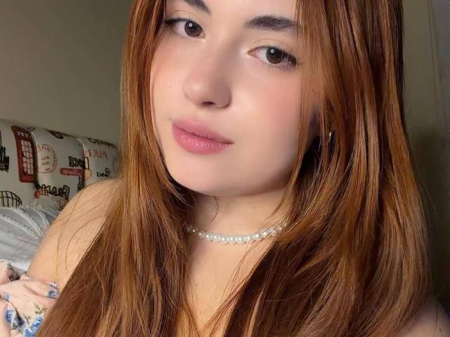 VicluX tem pele clara, olhos castanhos e cabelos longos castanhos, usando um colar de pérolas, com lábios rosados e um leve sorriso. Os seios não estão visíveis..