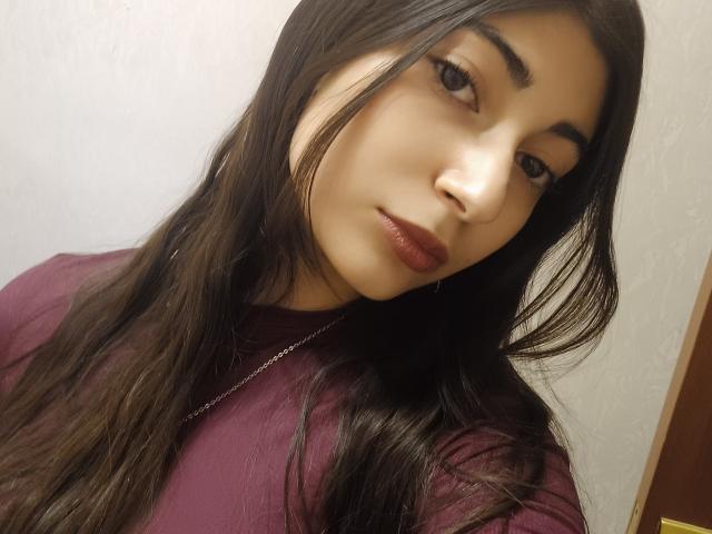 Onie Andreatta, con cabello castaño largo, cejas oscuras y lápiz labial burdeos, vestida con una blusa color burdeos, mirando ligeramente hacia un lado, con una sonrisa sutil..