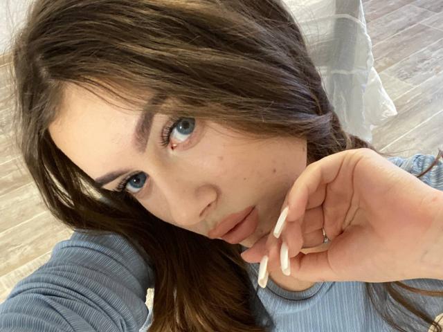Kimberly Zampieri, met lang bruin haar, blauwe ogen en bleke huid, leunt haar kin op haar hand, draagt een blauwe geribbelde top en laat haar lange, witte nagels zien..