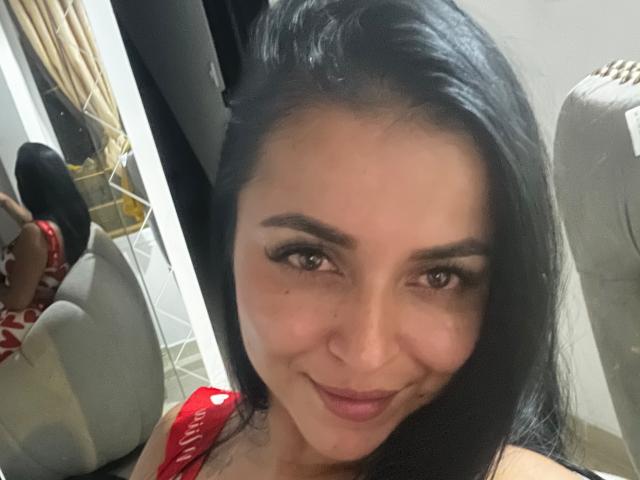HikariChloe tem cabelo preto e liso, olhos castanhos e um sorriso adorável. Ela está vestindo uma blusa vermelha com letras brancas, que mostra seus ombros e um pouco do colo..