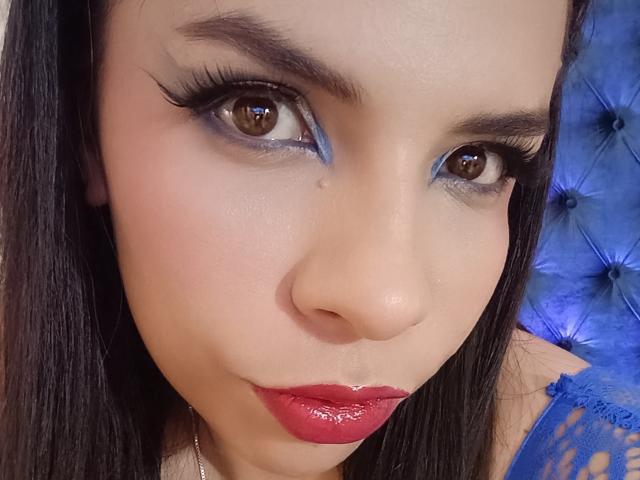 VioletaStone's face with glossy red lipstick, blue eyeliner, and thick eyelashes. She has brown eyes, dark straight hair, and a small beauty mark near her right eye.